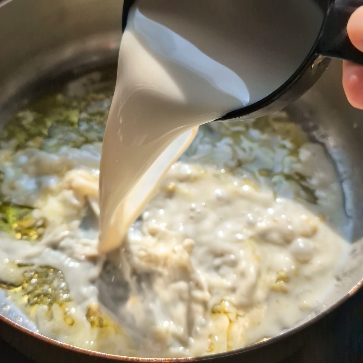 oat milk poured into a pan of garlic and olive oil to make a creamy vegan alfredo sauce.