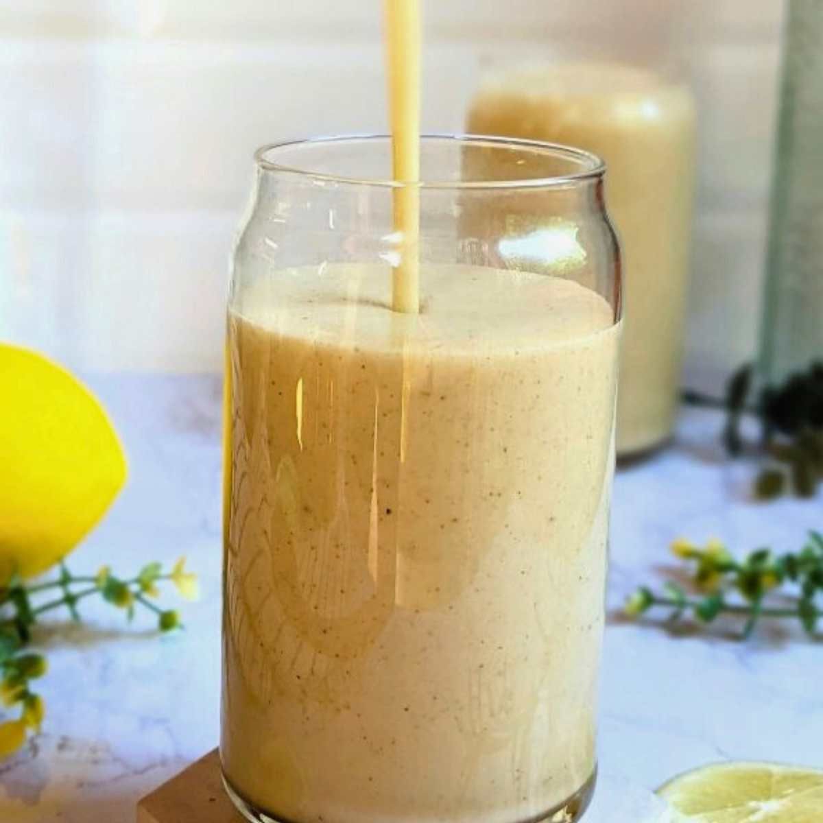 a tall can shaped glass being filled with a lemon smoothie with a light yellow color.