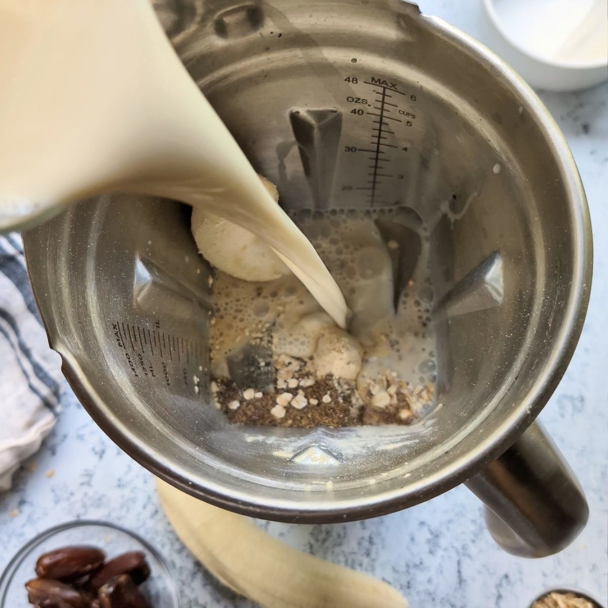 oat milk smoothie ingredients in a blender like bananas flaxseeds dates and oat milk being poured in.