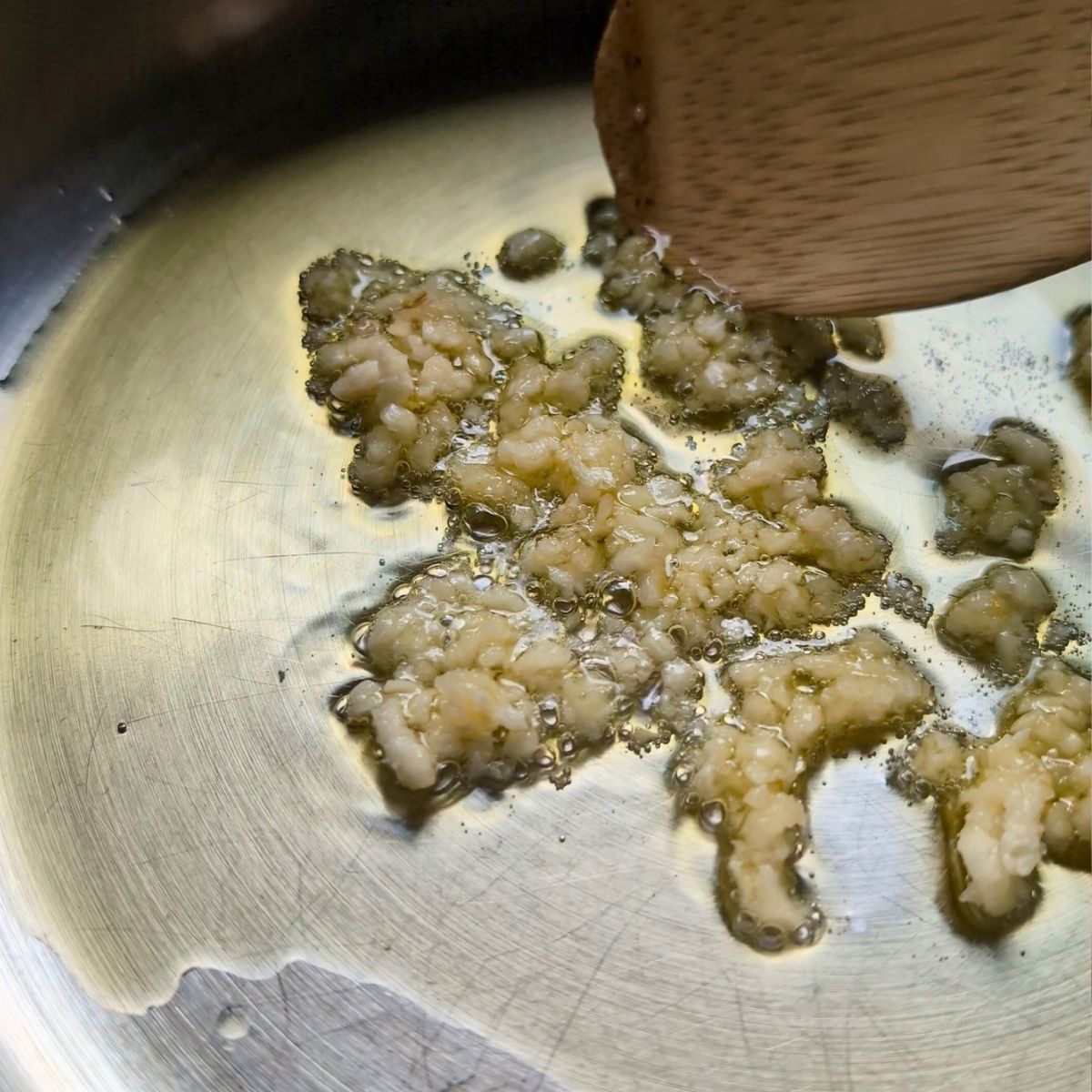 garlic and olive oil being sauteed in the pan being stirred by a wooden spoon.