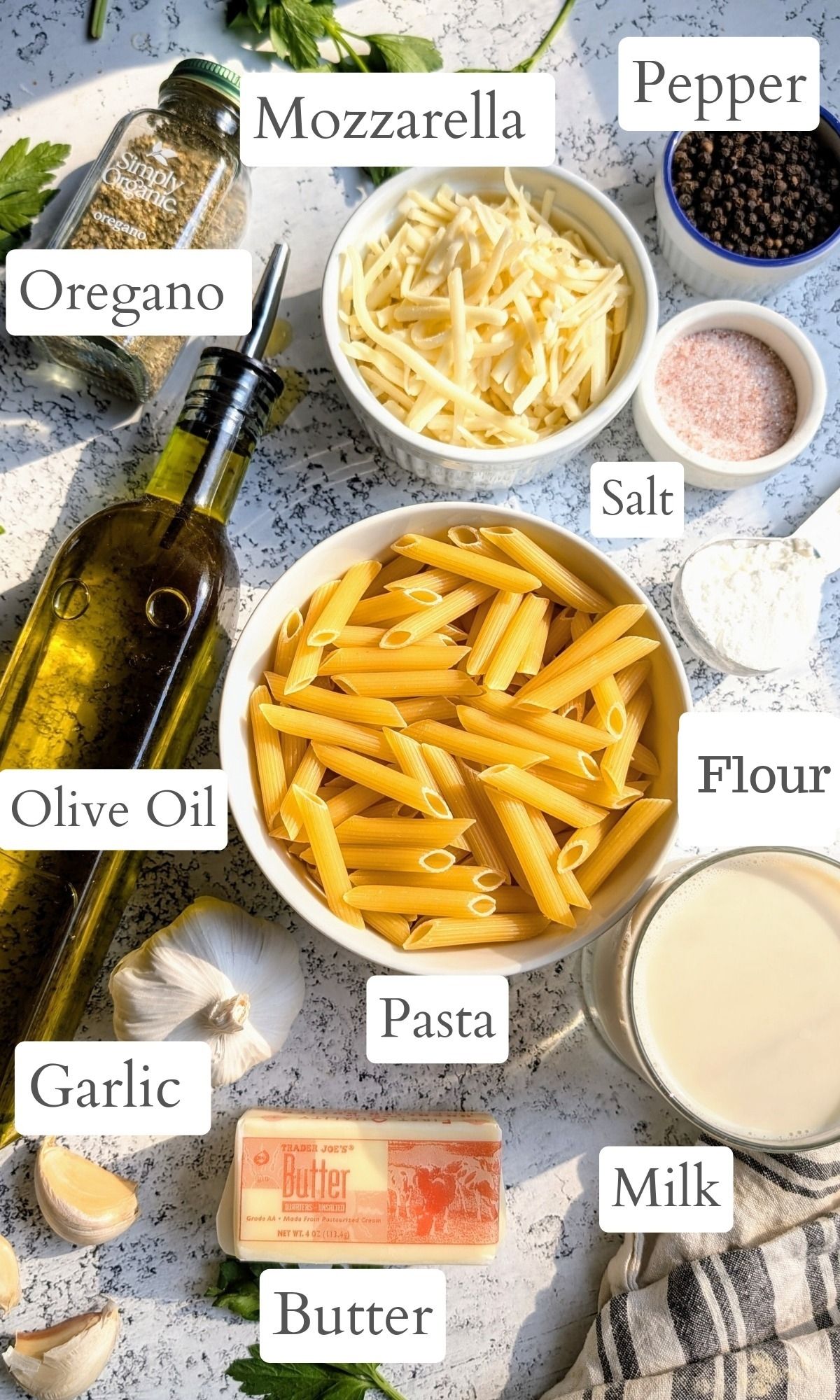 ingredients for a mozzarella alfredo pasta like penne noodles, olive oil, salt, flour, garlic, milk, and parsley.