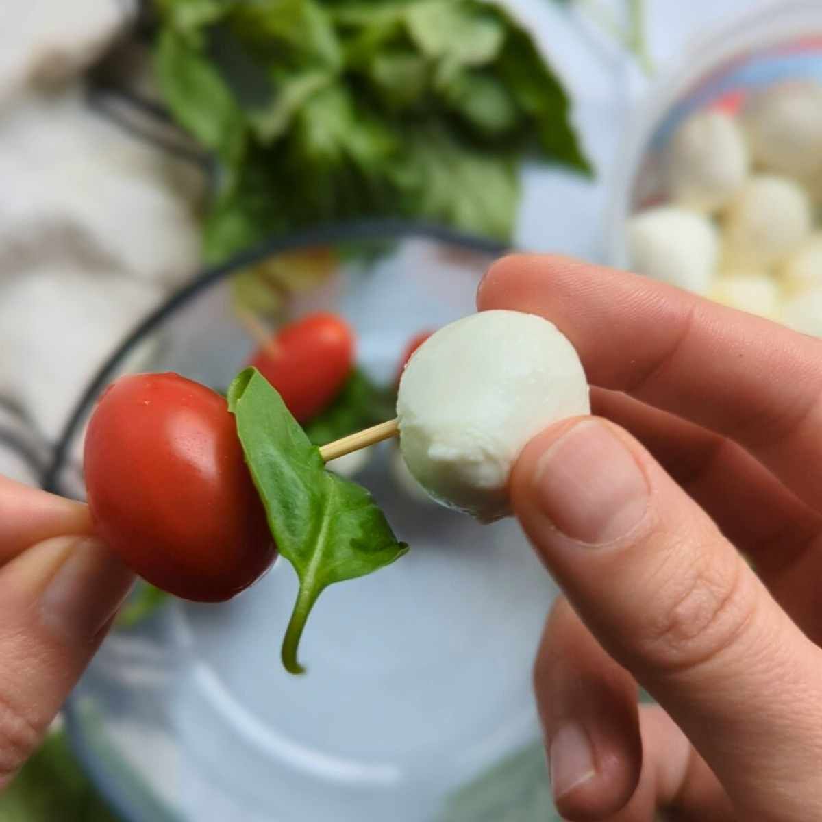 a piece of mozzarella being skewered onto a toothpick with fresh tomato and basil leaf.