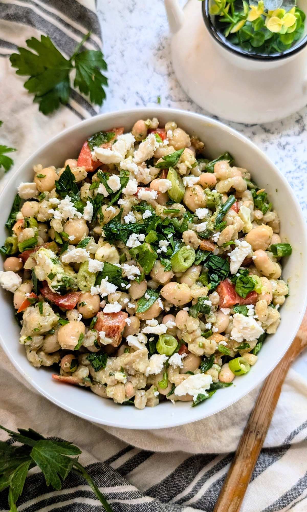 a large bowl of bean and barley salad topped with crumbled feta cheese and fresh parsley and green onions.