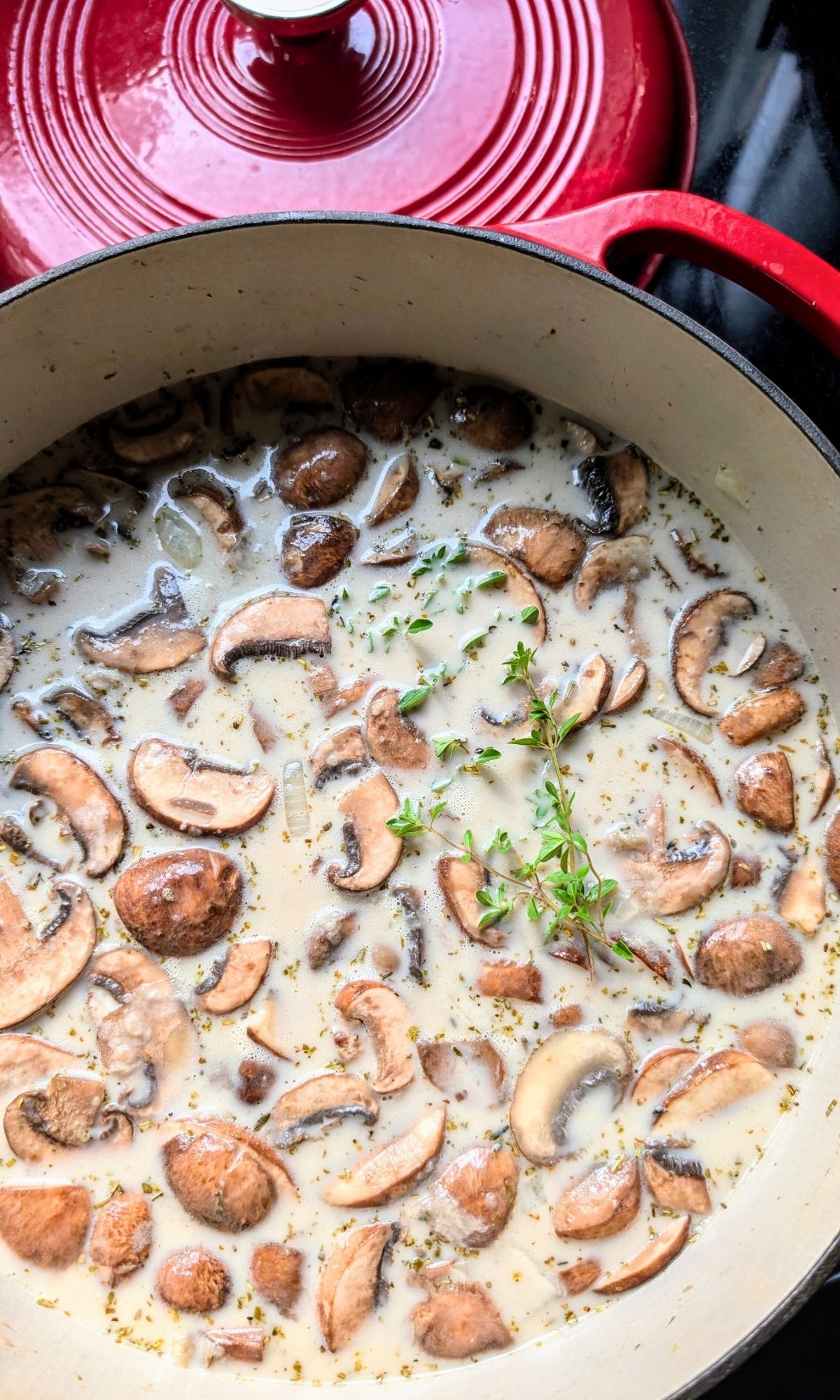 a large pot of mushroom soup with coconut milk topped with fresh herbs.