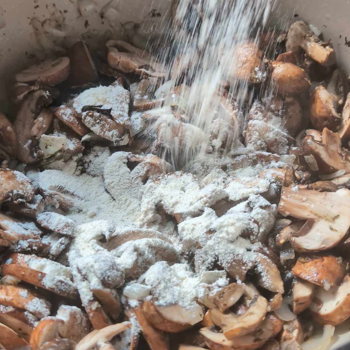 flour being sprinkled onto chopped mushrooms in a pan to thicken the soup.