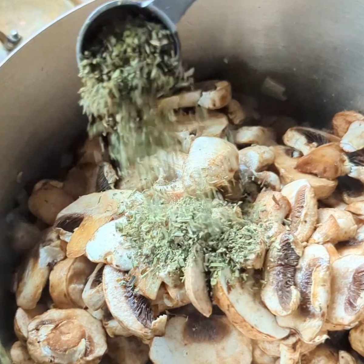 a pan full of mushrooms and fresh herbs being added to the pot while cooking a soup.