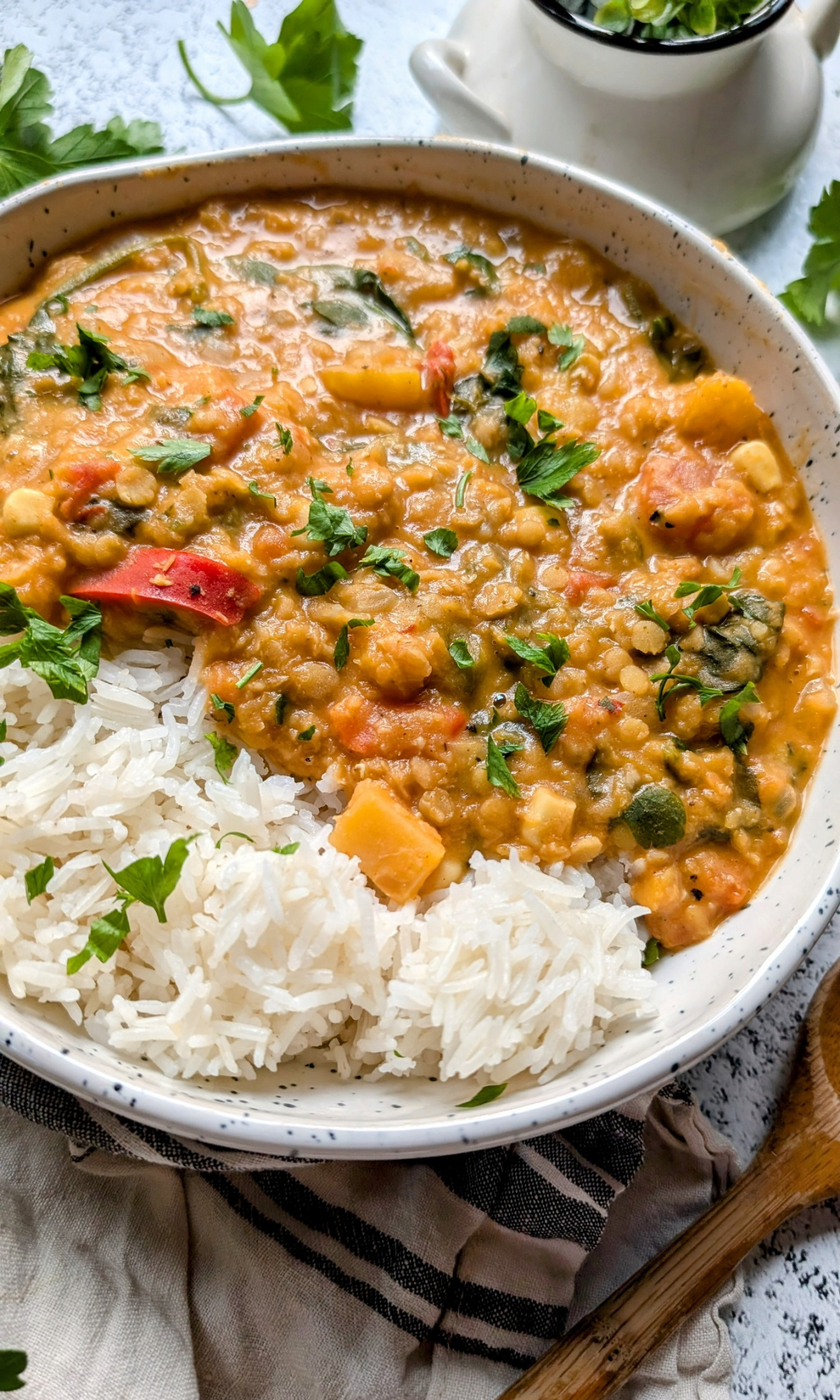 a large bowl of red lentil dahl with butternut squash and red peppers served over white basmati rice in a bowl.