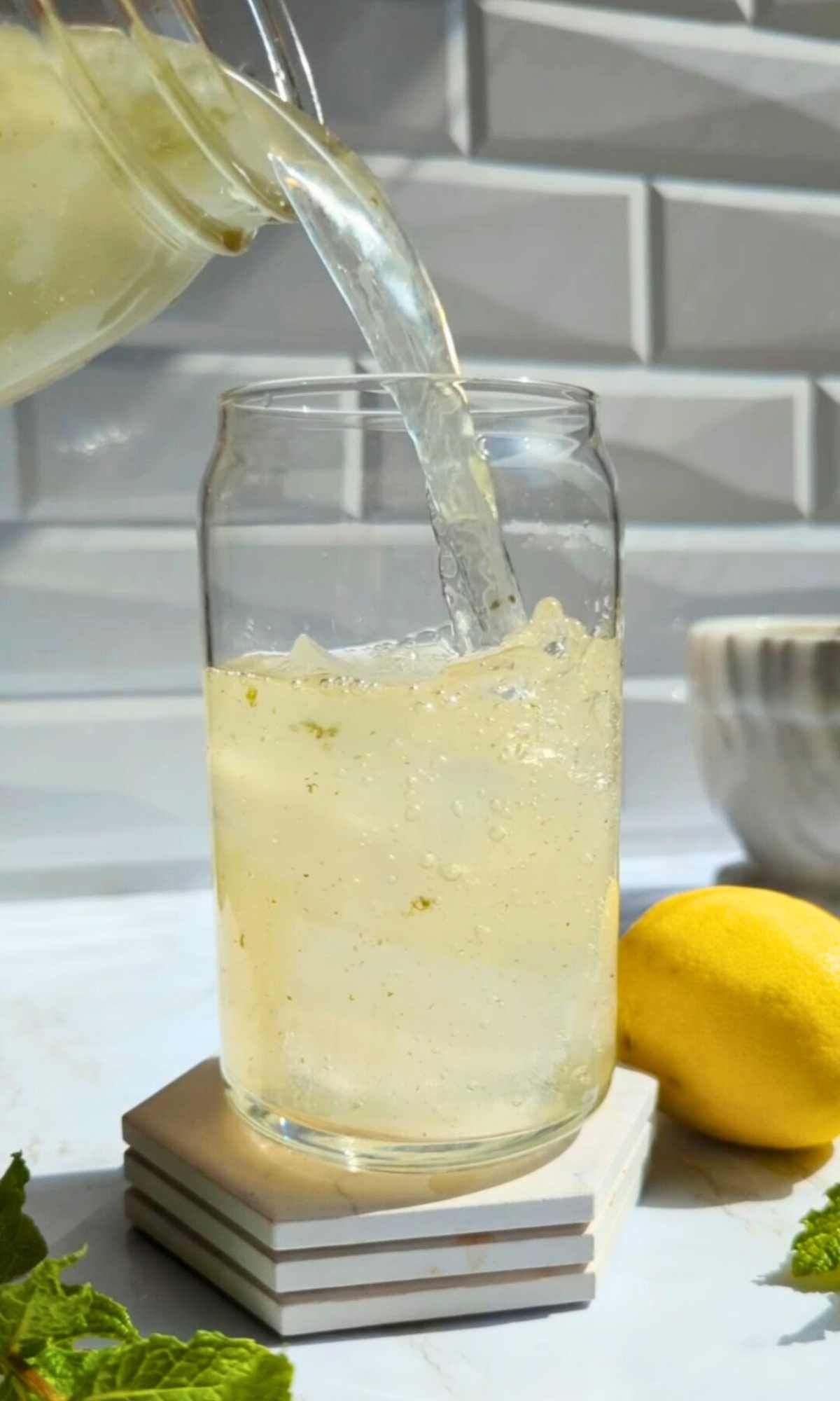 fresh homemade mint lemonade being poured into a glass over ice cubes on a hot summer day.