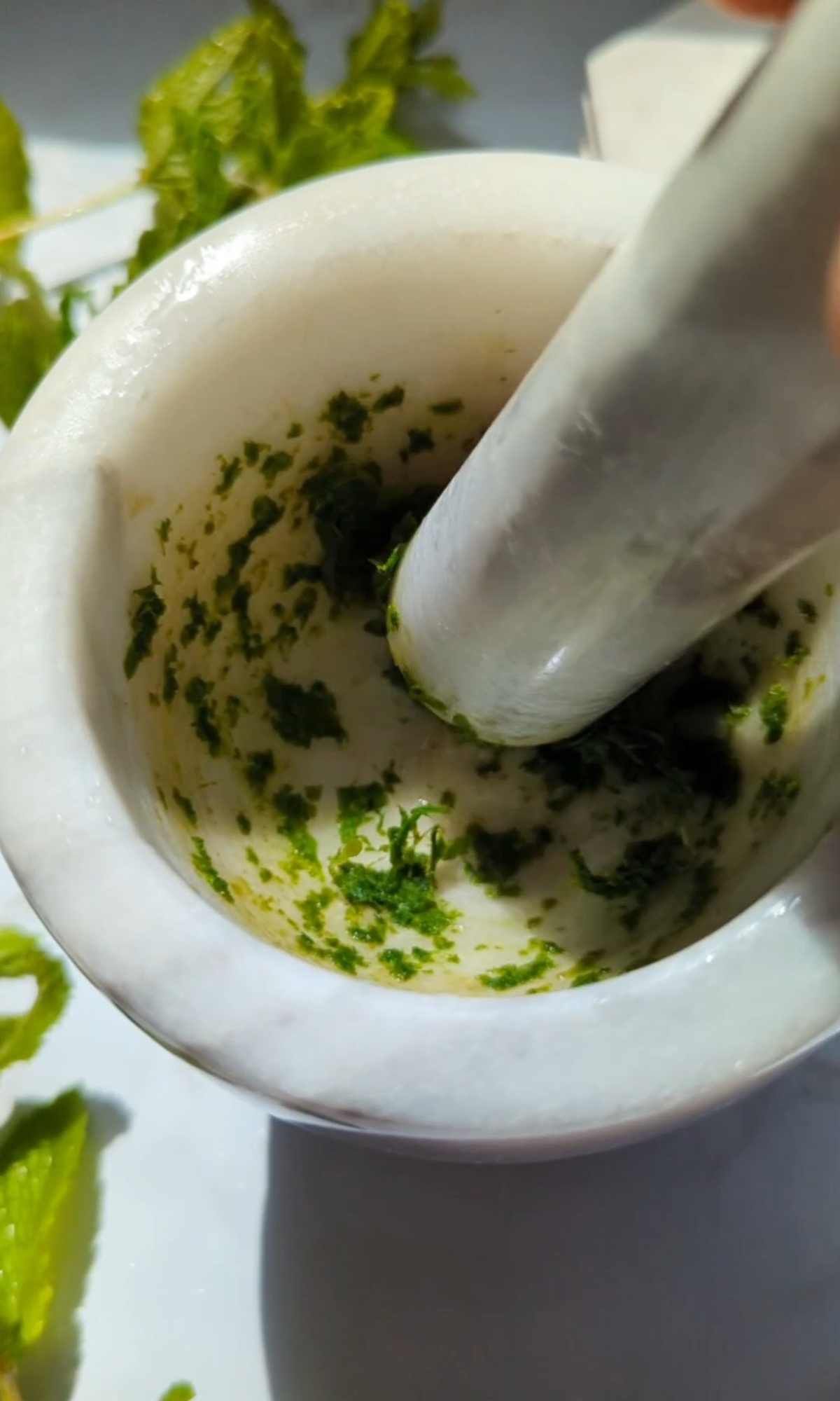 fresh mint leaves being muddled in a mortar and pestle to make lemonade.