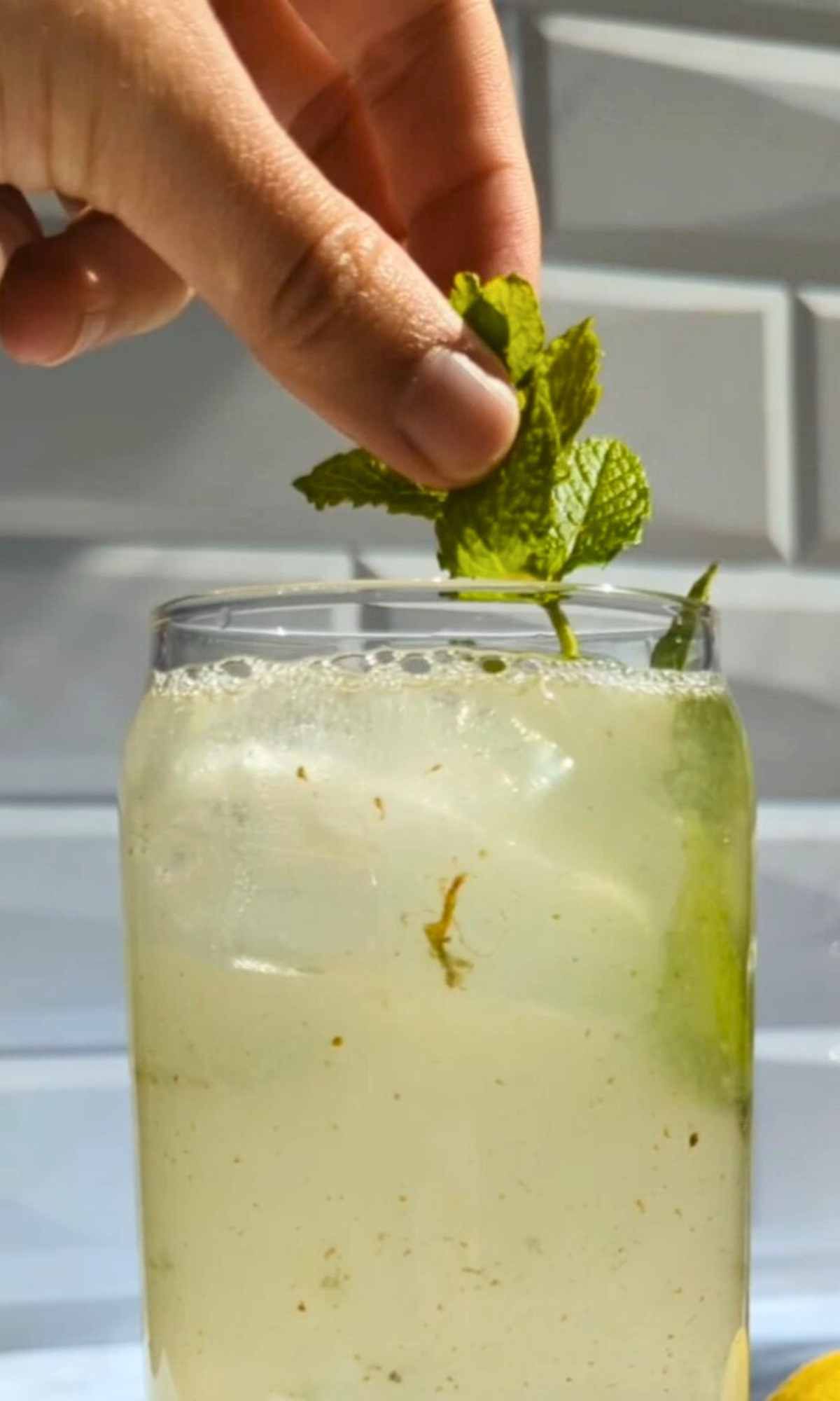 a hand garnishing homemade lemonade with mint leaves from the garden.