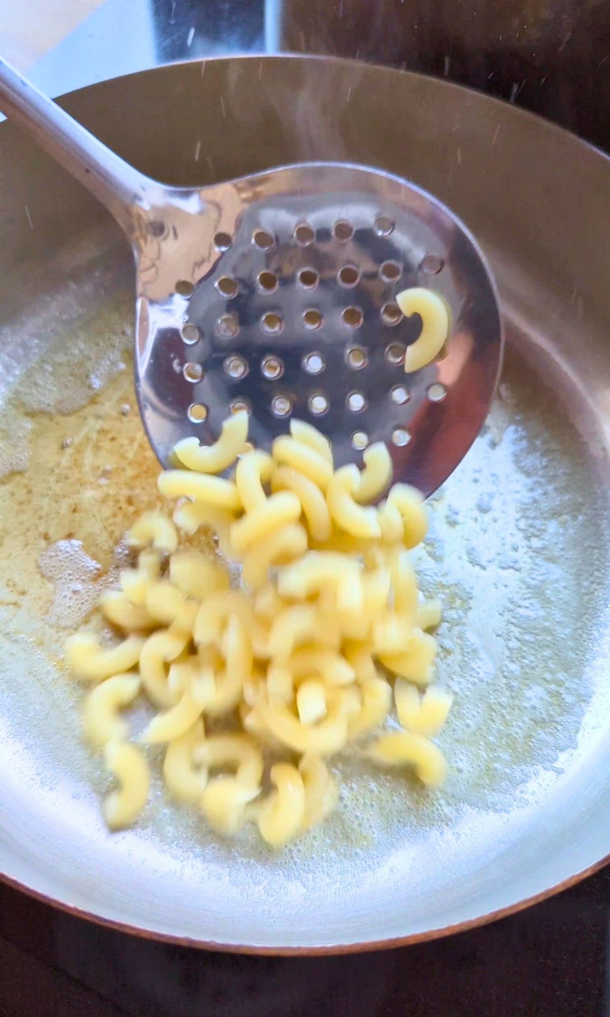 cooked macaroni noodles being added to melted butter in a pan.