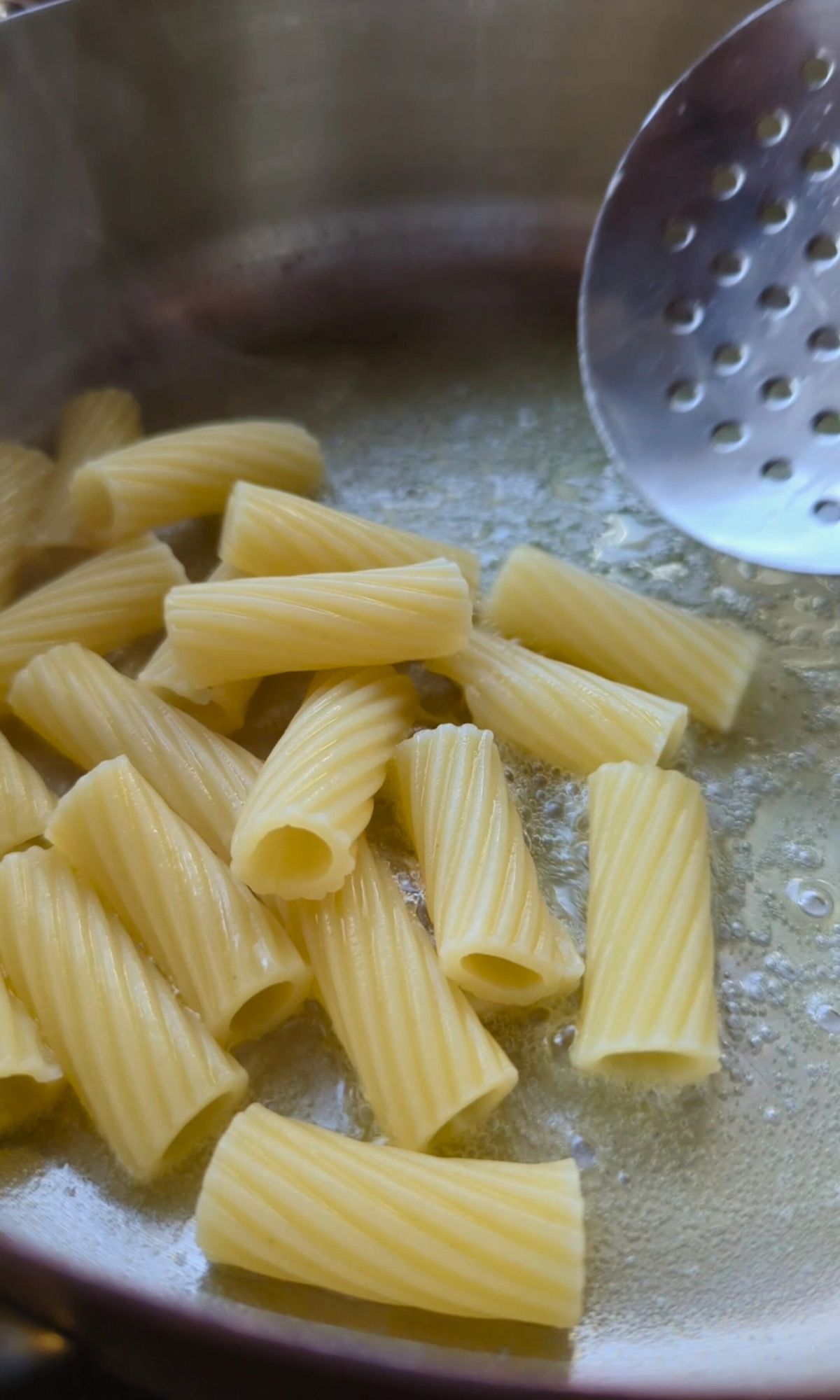 adding cooked rigatoni pasta noodles in a pan with melted butter.