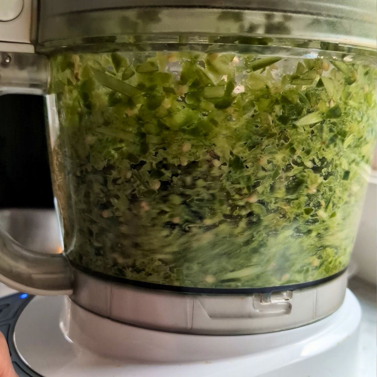 a food processor with garlic scapes, peppers, and vinegar being blended into a hot sauce.