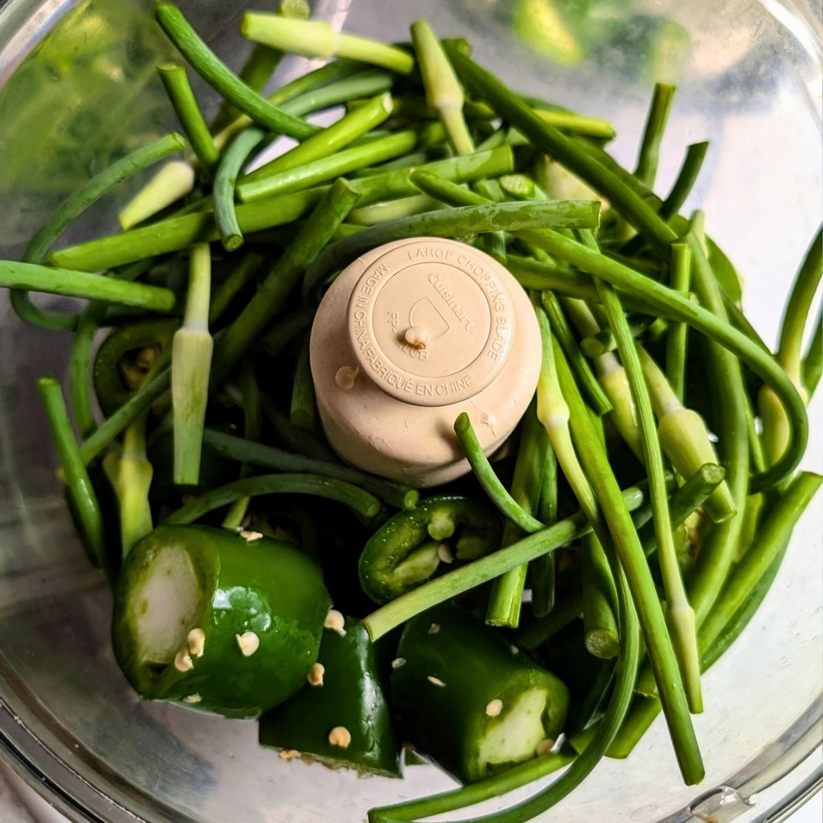 a food processor with equal parts garlic scapes and jalapeno peppers