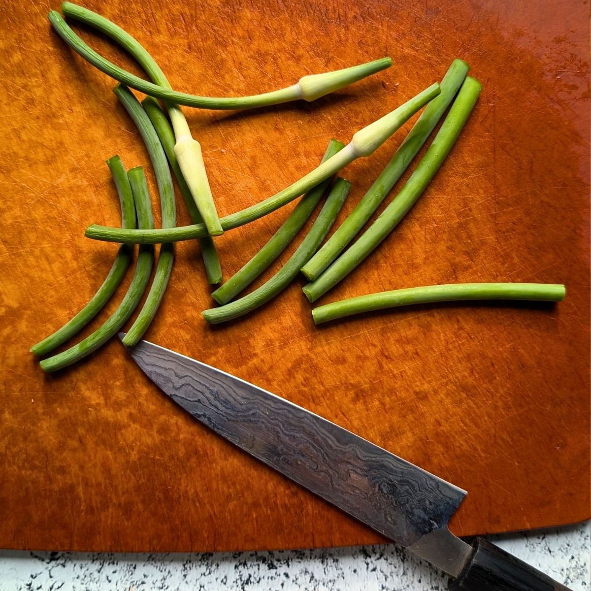 trimmed garlic scapes with tough stems removed on a cutting board.