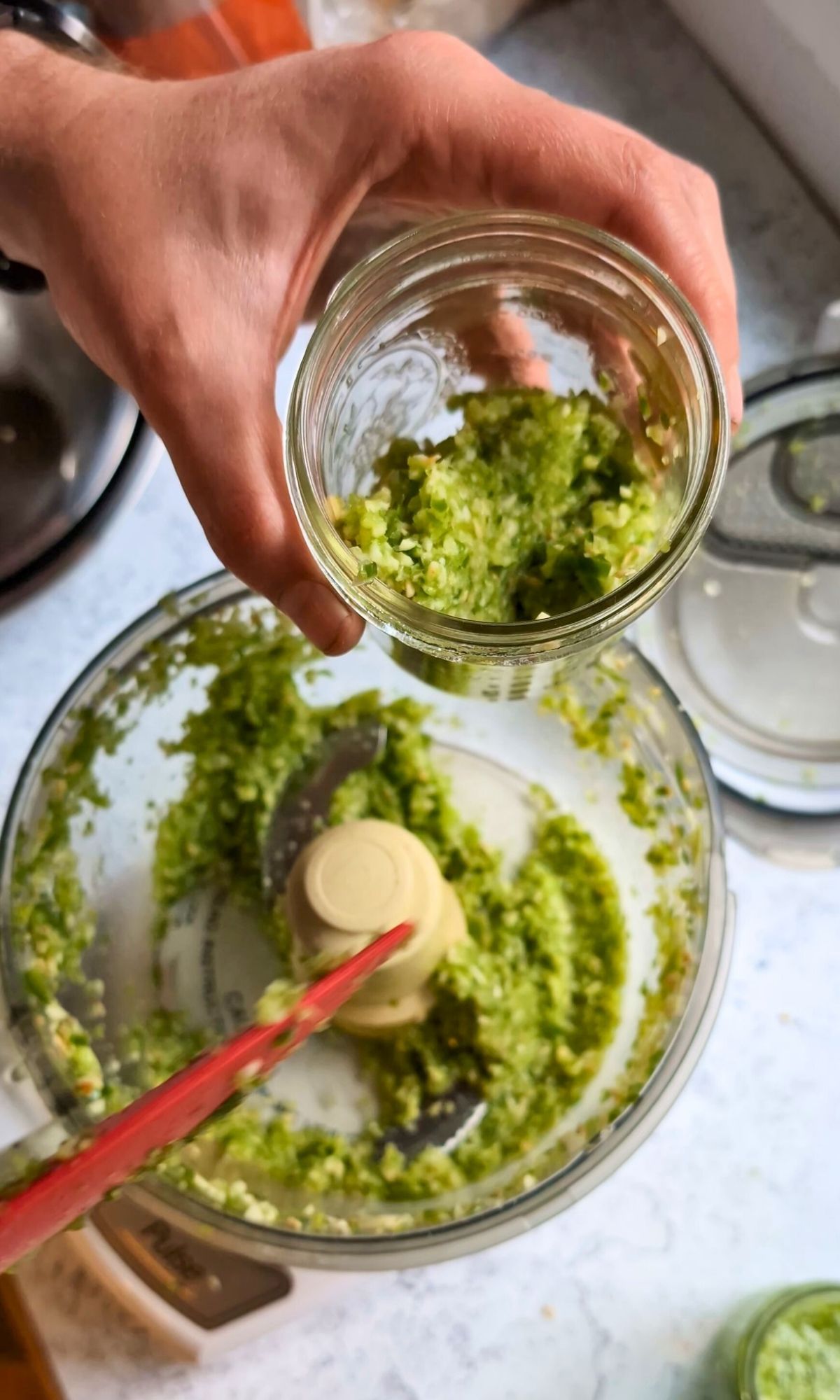 a spatula scraping peppers and garlic scapes into a jar for a chunky hot sauce.