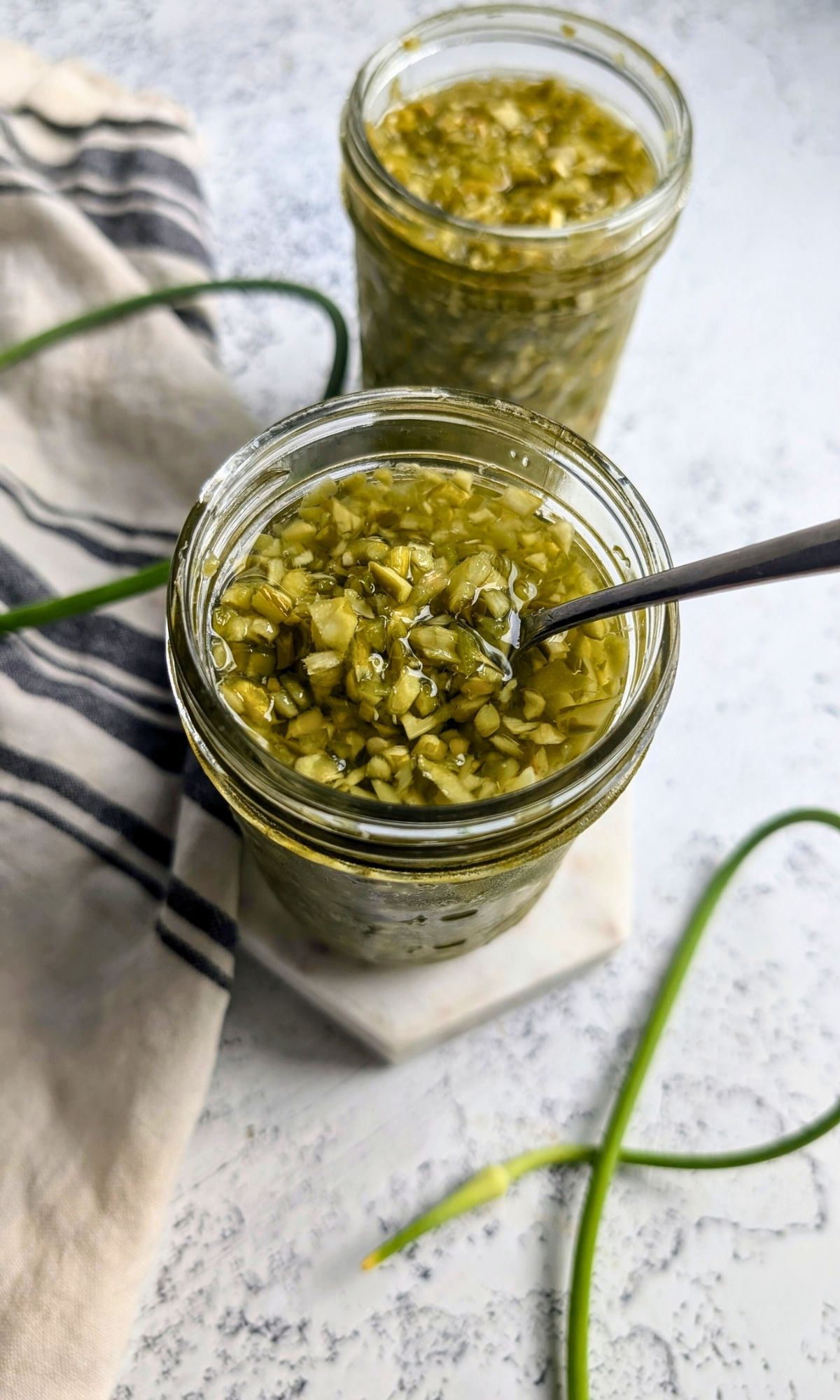 a spoon scooping hot sauce with garlic scapes and peppers.