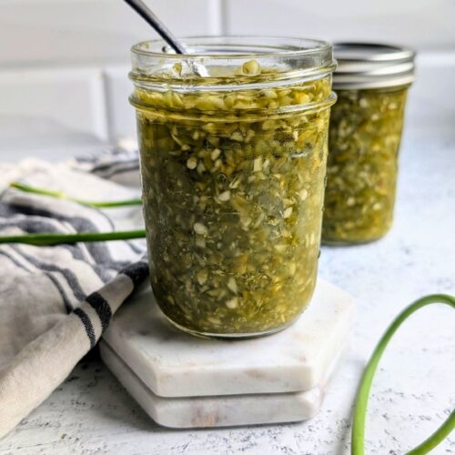 garlic scape hot sauce recipe with fresh scapes and jalapeno peppers in a jar with a spoon.