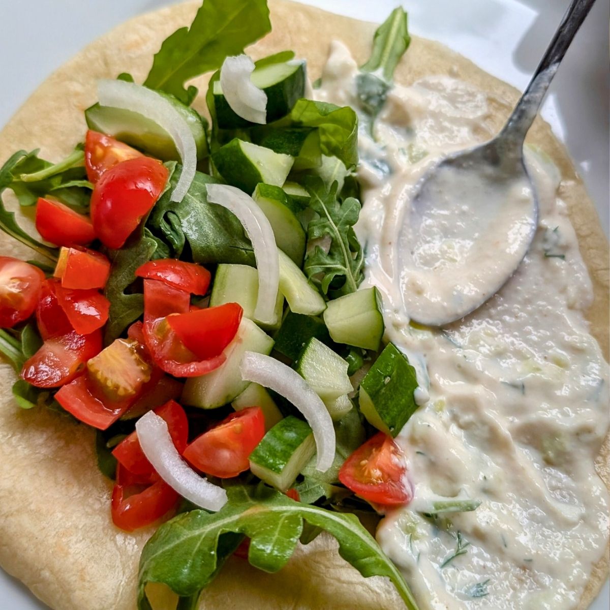 a pita bread with vegan garlic sauce, tomatoes, greens, cucumber, and onion.