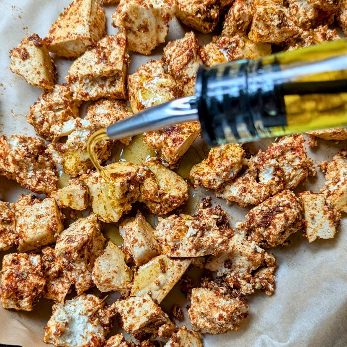 shawarma tofu on a sheetpan being tossed with olive oil to make it crispy in the oven.