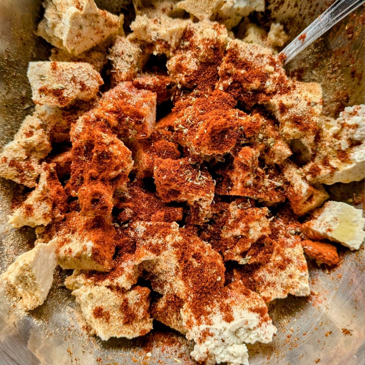 A bowl with crumbled tofu and paprika, coriander, onion powder, and chili powder.