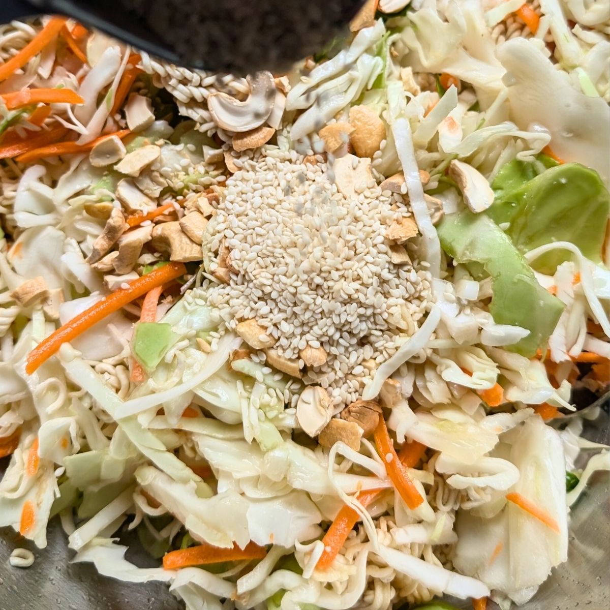 peanuts and sesame seeds being added to a coleslaw salad with crushed ramen noodles.