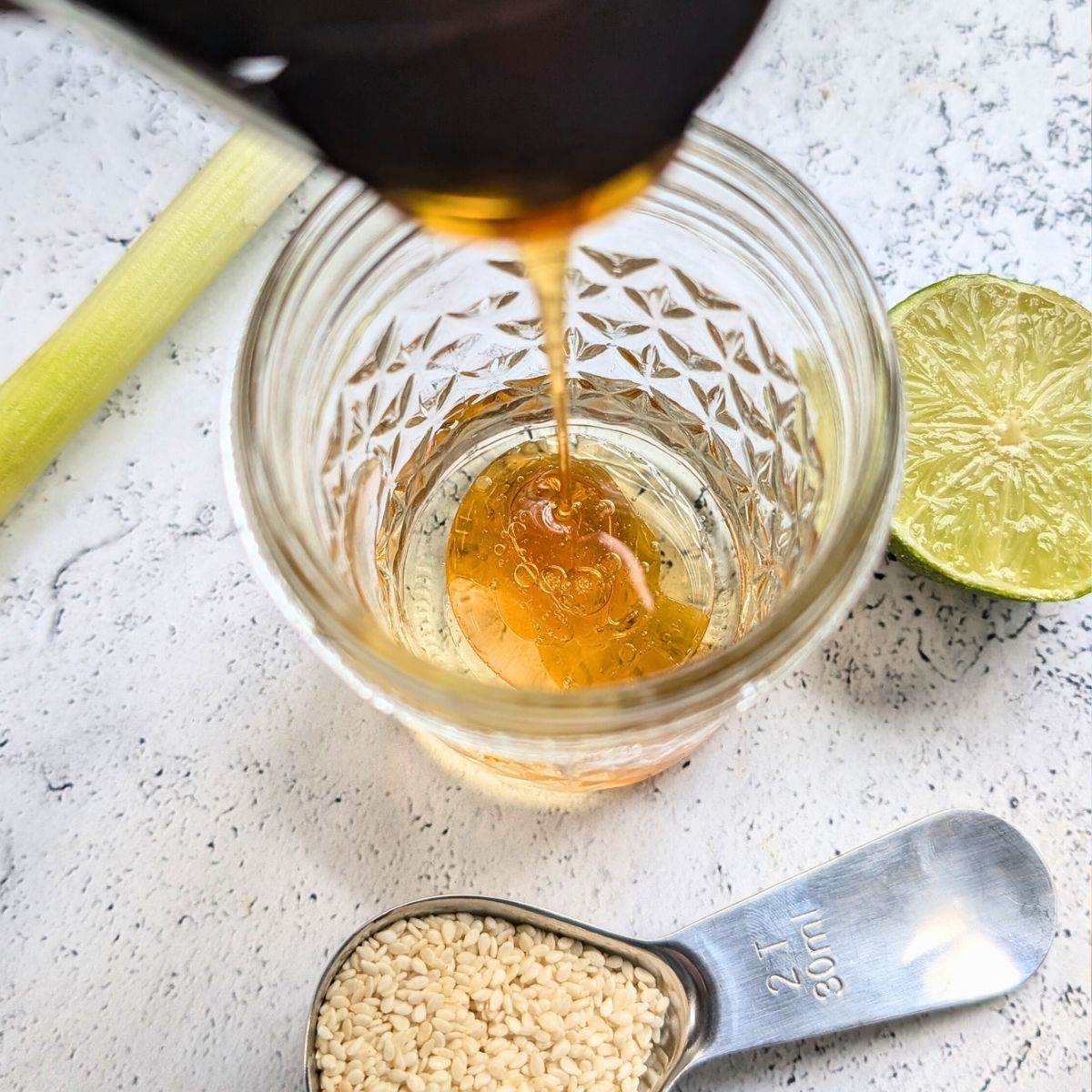 a mason jar being filled with ramen salad dressing ingredients like maple syrup, lime juice, sesame oil, and olive oil.