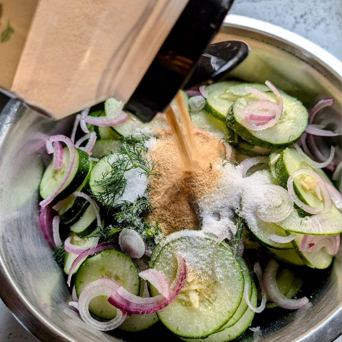 a large bowl of cucumber salad with sugar and garlic powder being poured into the salad for the dressing.