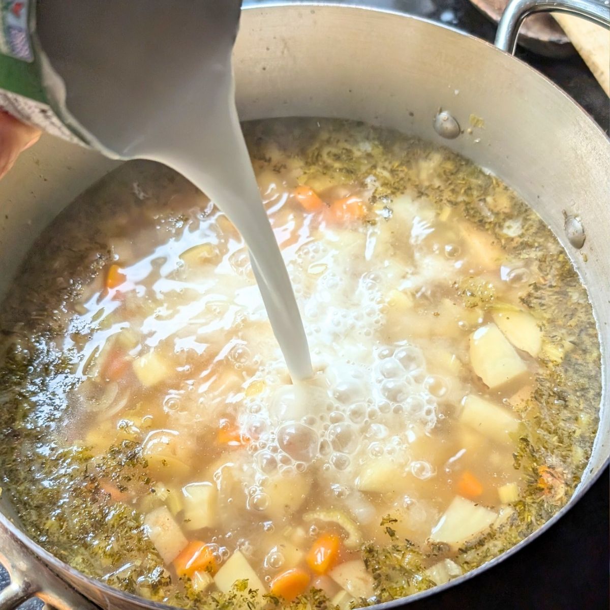 coconut milk being poured into a large pot of potato soup for a tasty creamy and dairy free dinner idea.