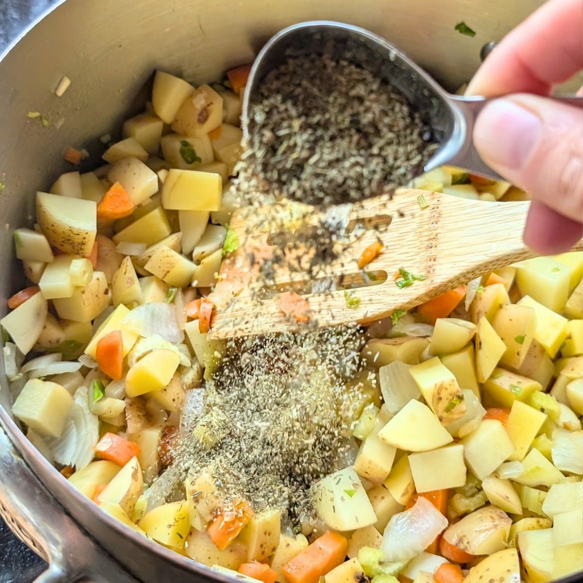 potatoes and thyme being added to a pot with the vegetables to make dairy free coconut potato soup.