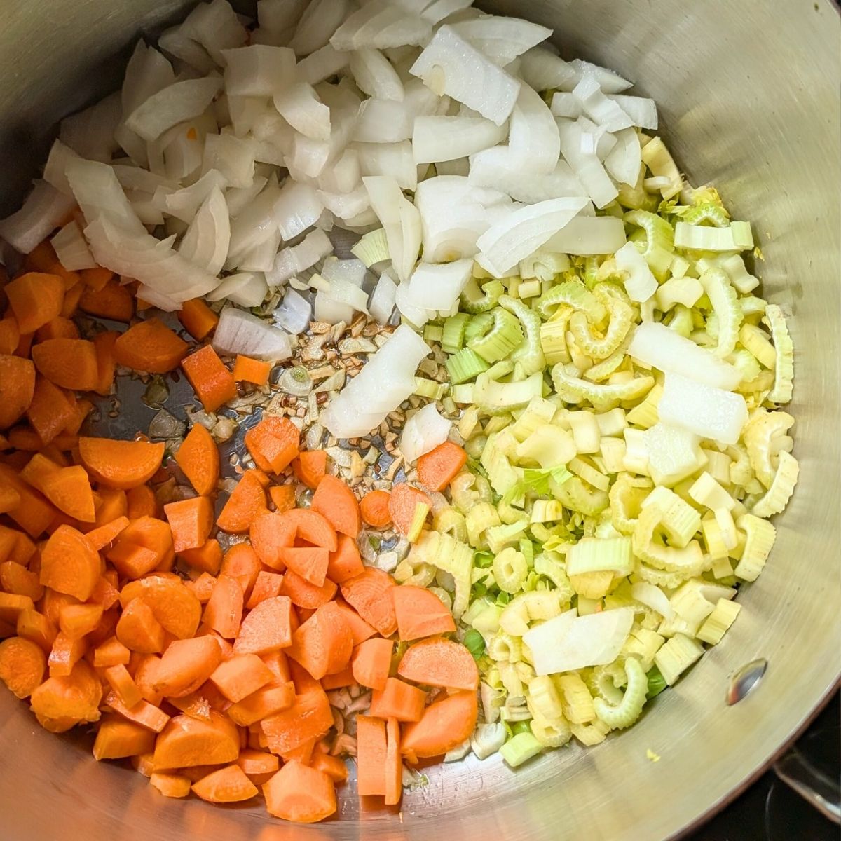 a soup pot with the holy trinity vegetables of onions, celery, and carrots for potato soup.