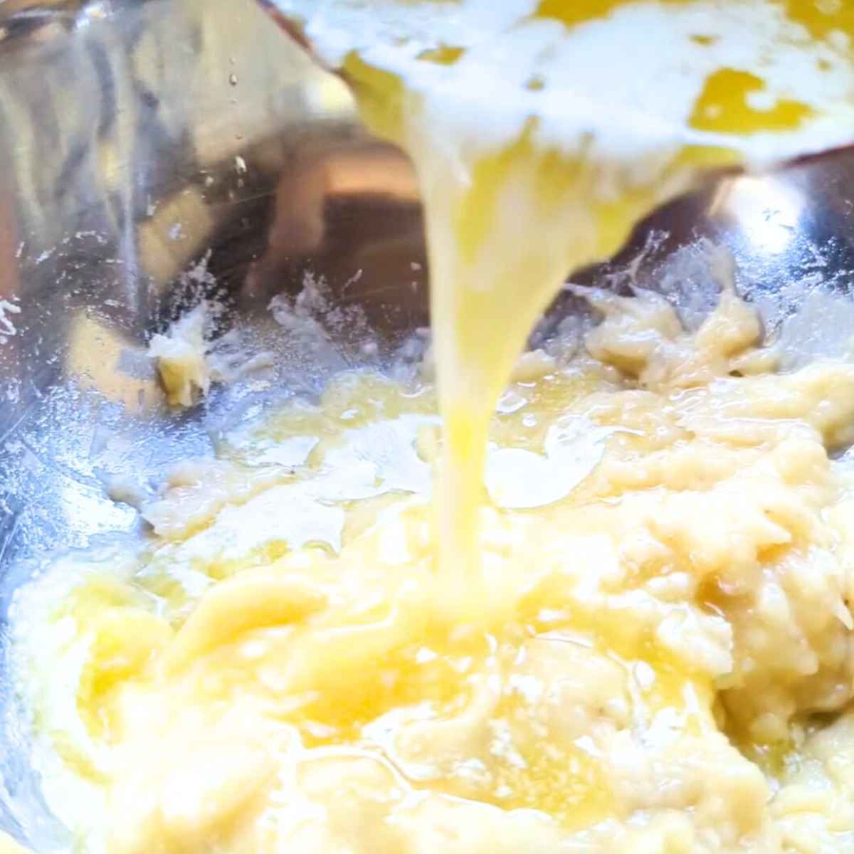 a mxing bowl with wet ingredients for banana bread: mashed bananas, eggs, milk, and melted butter.