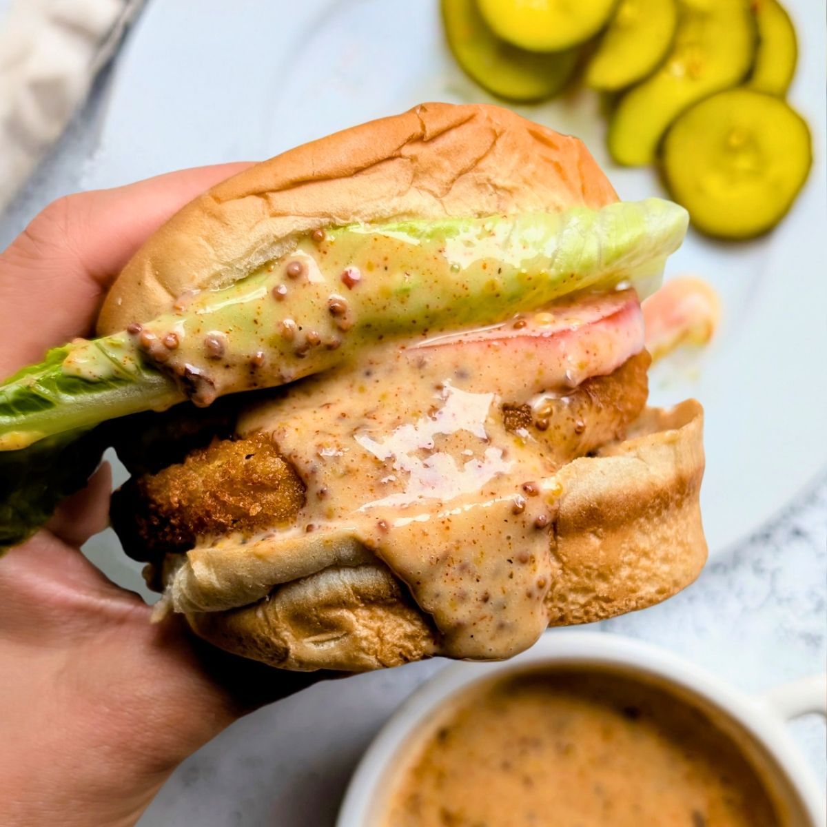 chicken sandwich sauce recipe with honey mustard mayo spices paprika and spicy chili flakes in a ramekin drizzled on a chicken sandwich with a honey dipper.