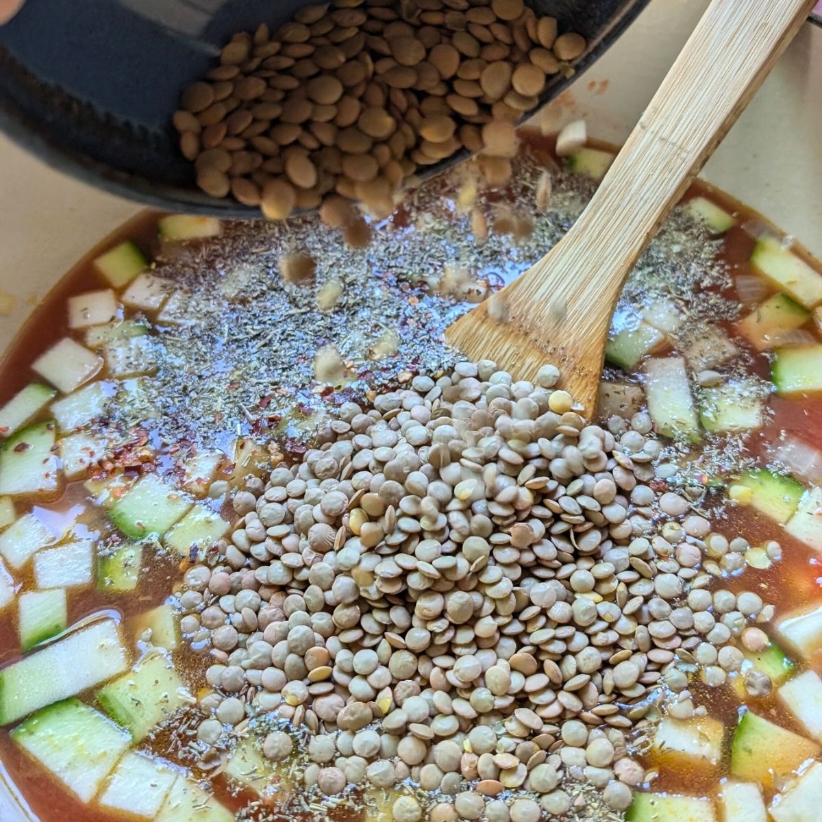 a pot of vegetables for soup with green lentils being added to the pot for a tasty homemade soup recipe.