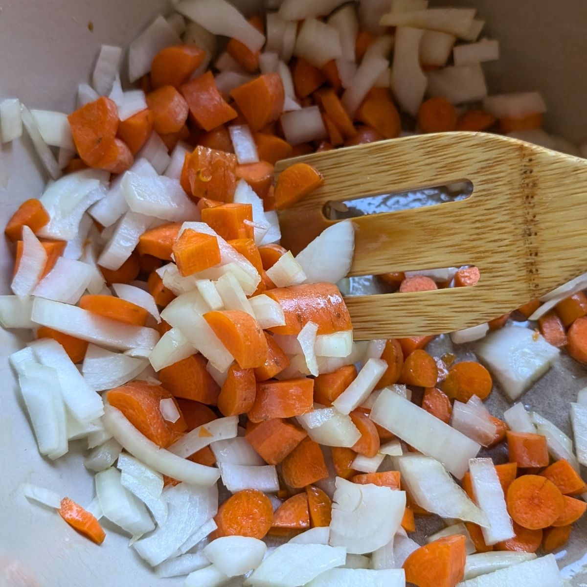 a soup pot with carrots, white onions, and garlic being sauteed in olive oil for soup.