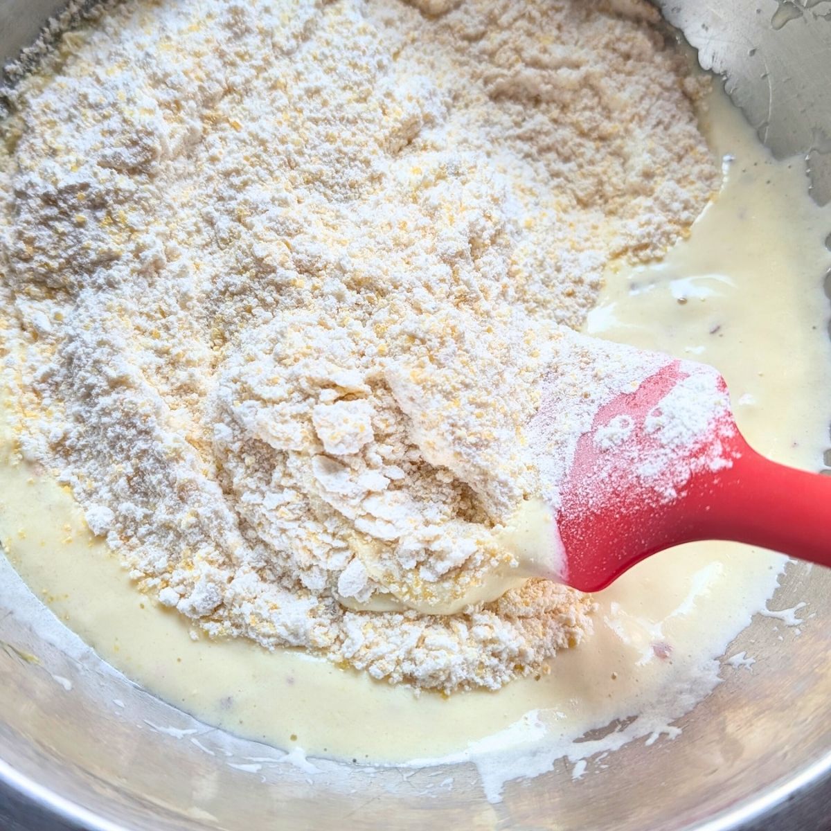 wet and dry ingredients for cornbread in a bowl bring mixed with a spatula.