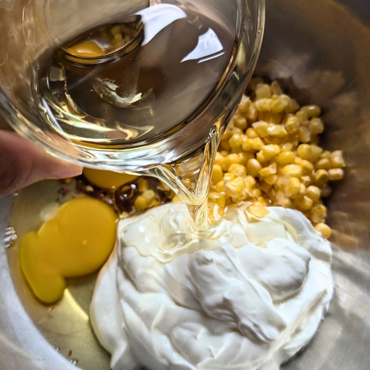 wet ingredients for cornbread in a bowl: greek yogurt, eggs, corn, and oil.