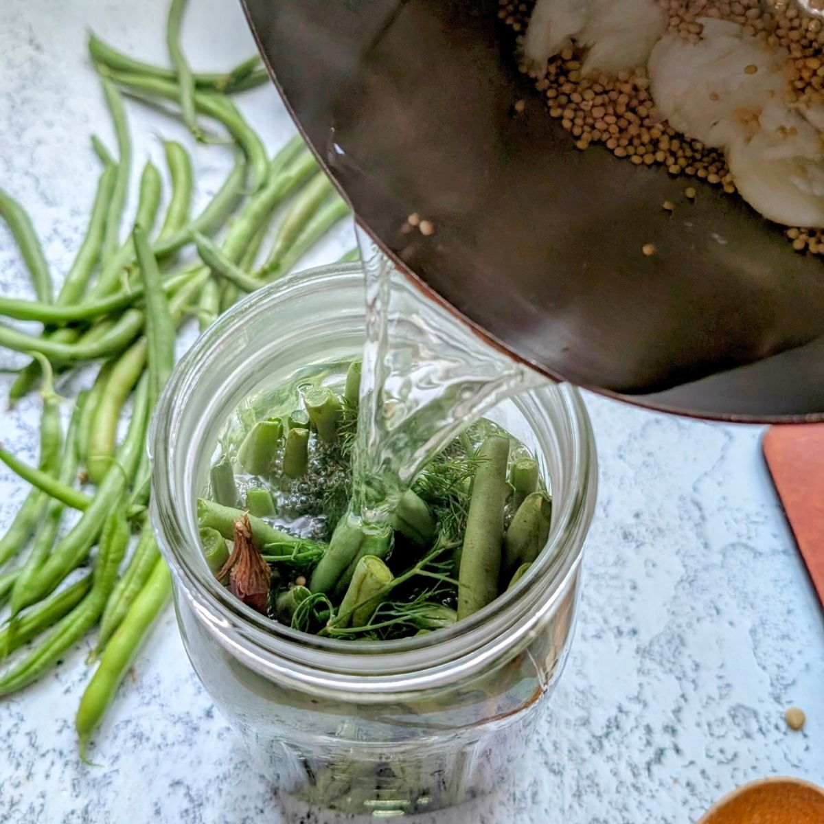 brine being poured into a jar of fresh summer green beans to make spicy pickled beans.