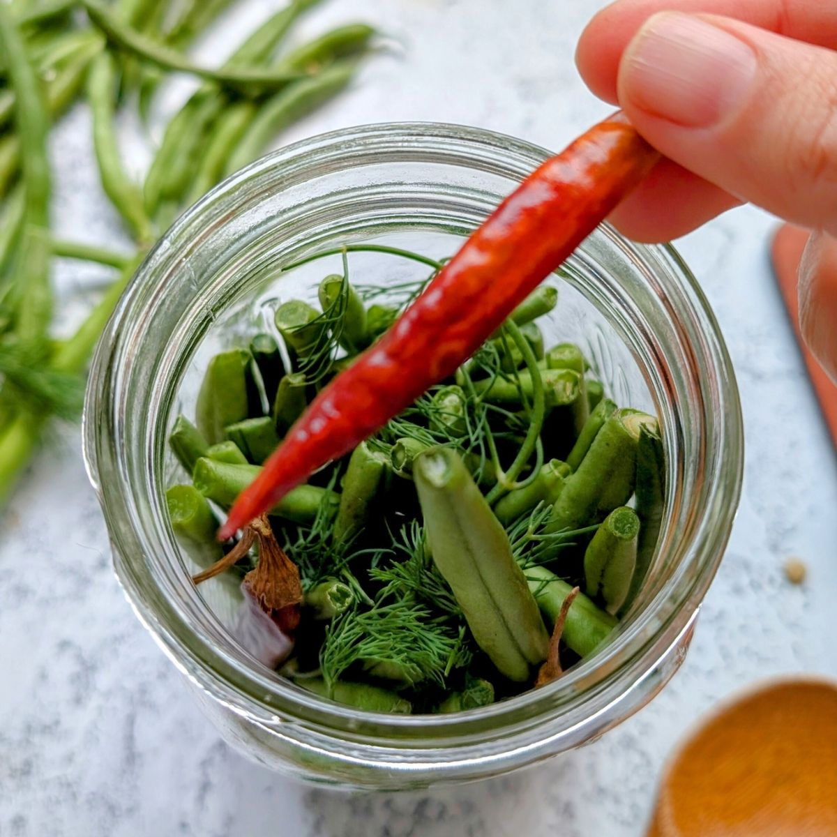 a hand placing a fried chili pepper into a jar of pickled beans.