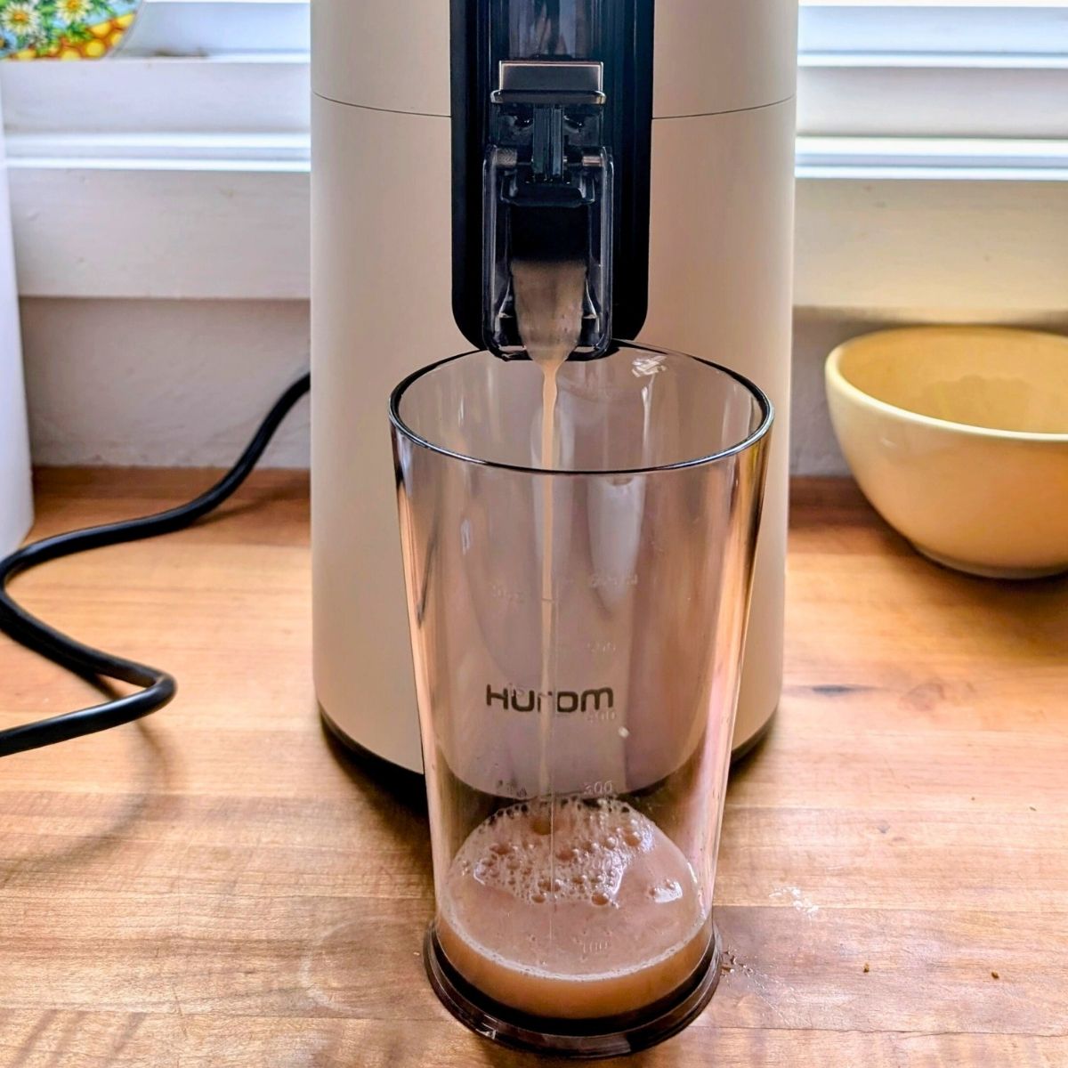 a hurom juicer making plum juice on a kitchen counter with butcherblock wood countertops.