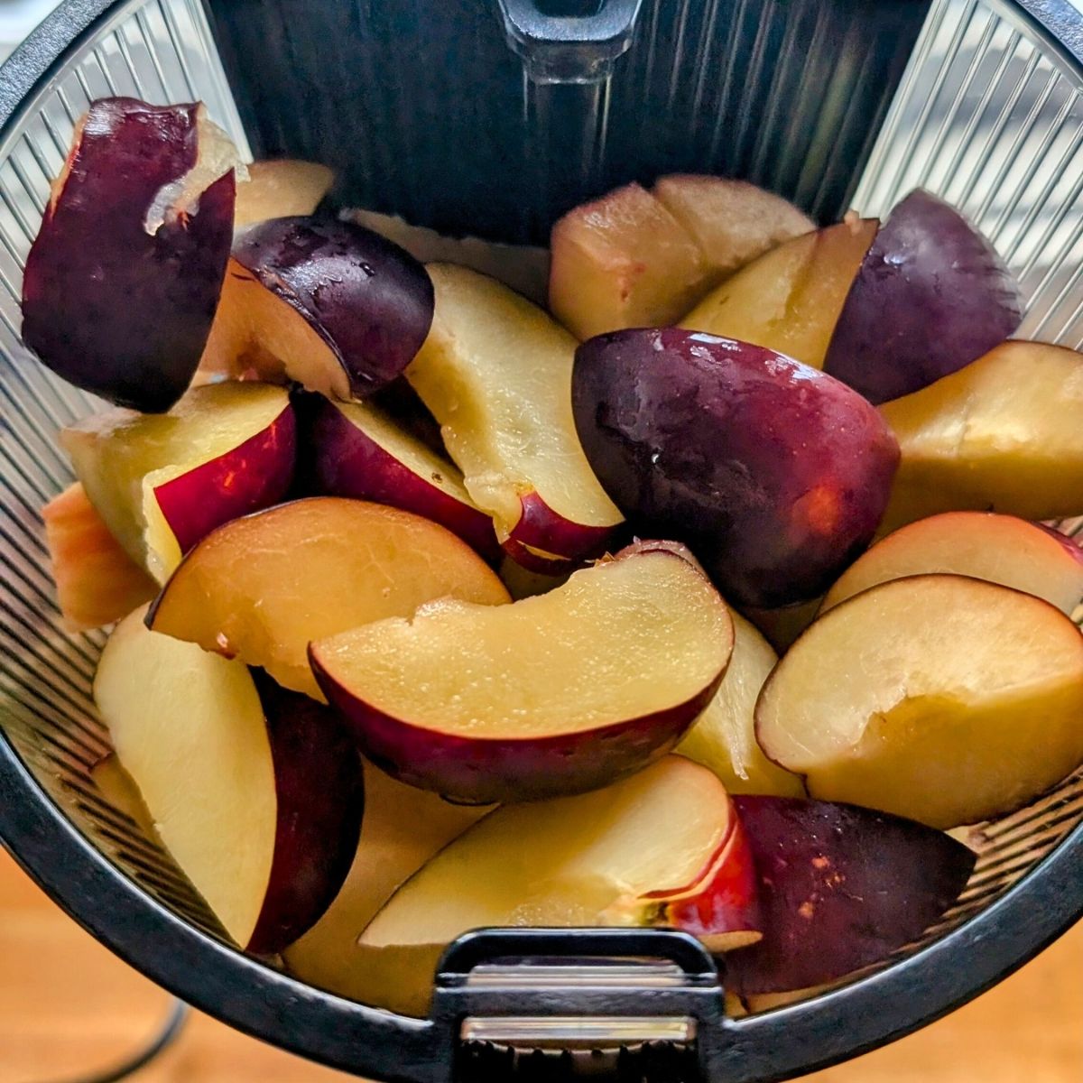 a juicer hopper full of fresh sliced plums and apples with lime juice, a hurom bulk juicer.