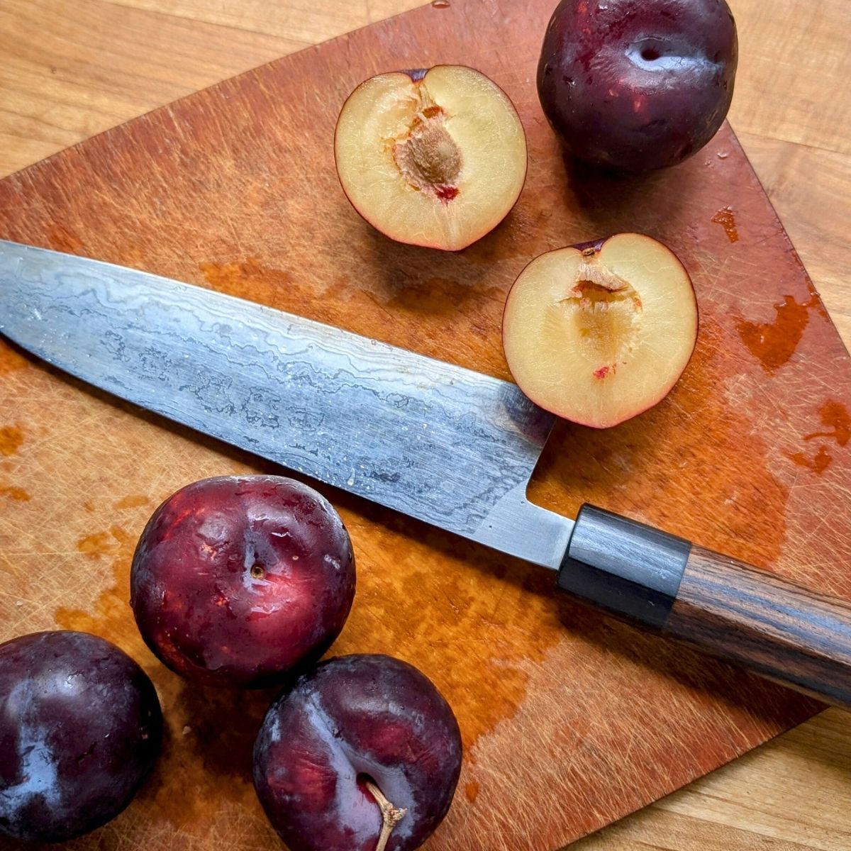 a japanese knife slicing up fresh plums with yellow flesh on a cutting board.