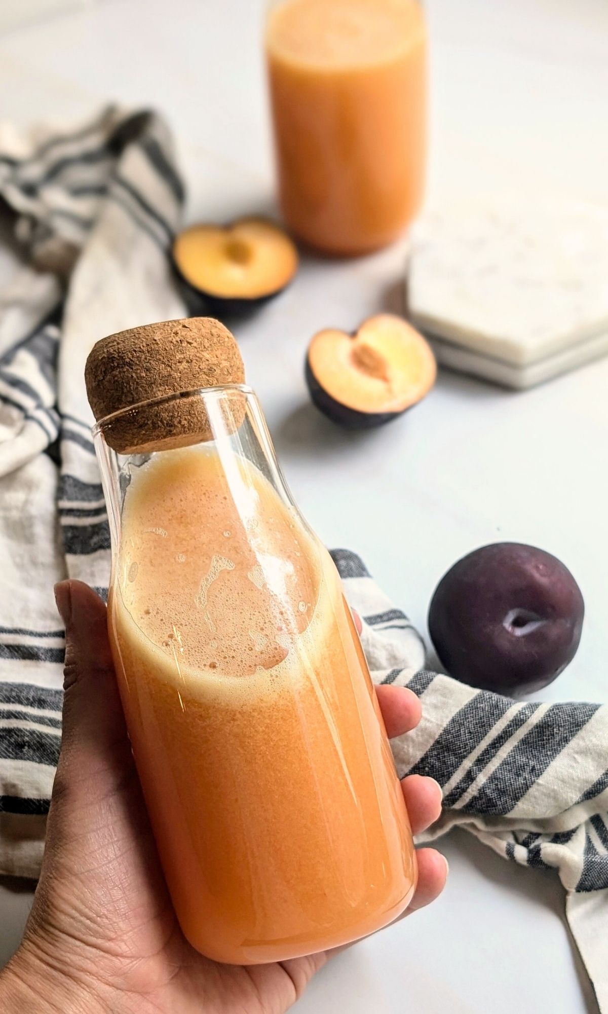 a hand holding a bottle of freshly juiced plum and apple juice with lime.