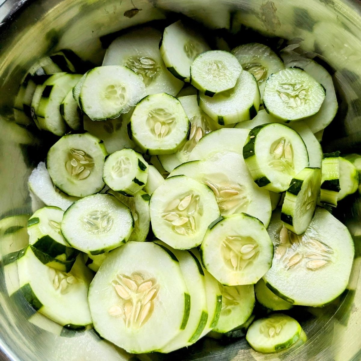 sliced cucumbers in a bowl that are half peeled and thinly sliced.