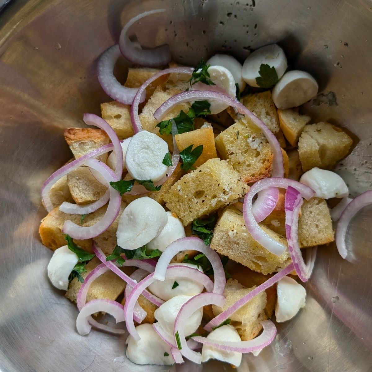 a large bowl with toasted sourdough, sliced red onion, parsley, and fresh mozzarella cheese.