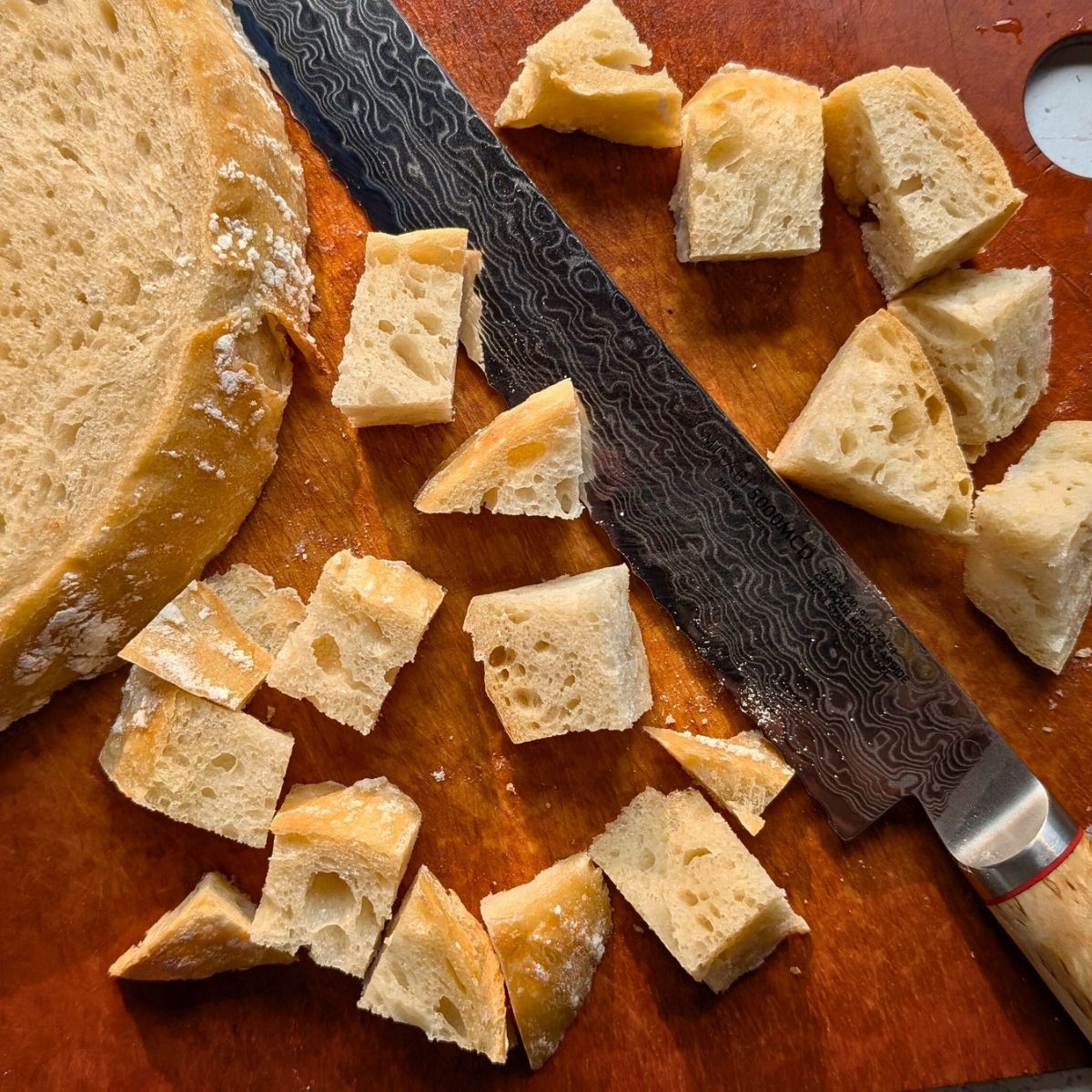 sliced sourdough bread is cubed with a bread knife on a counter for panzanella salad.