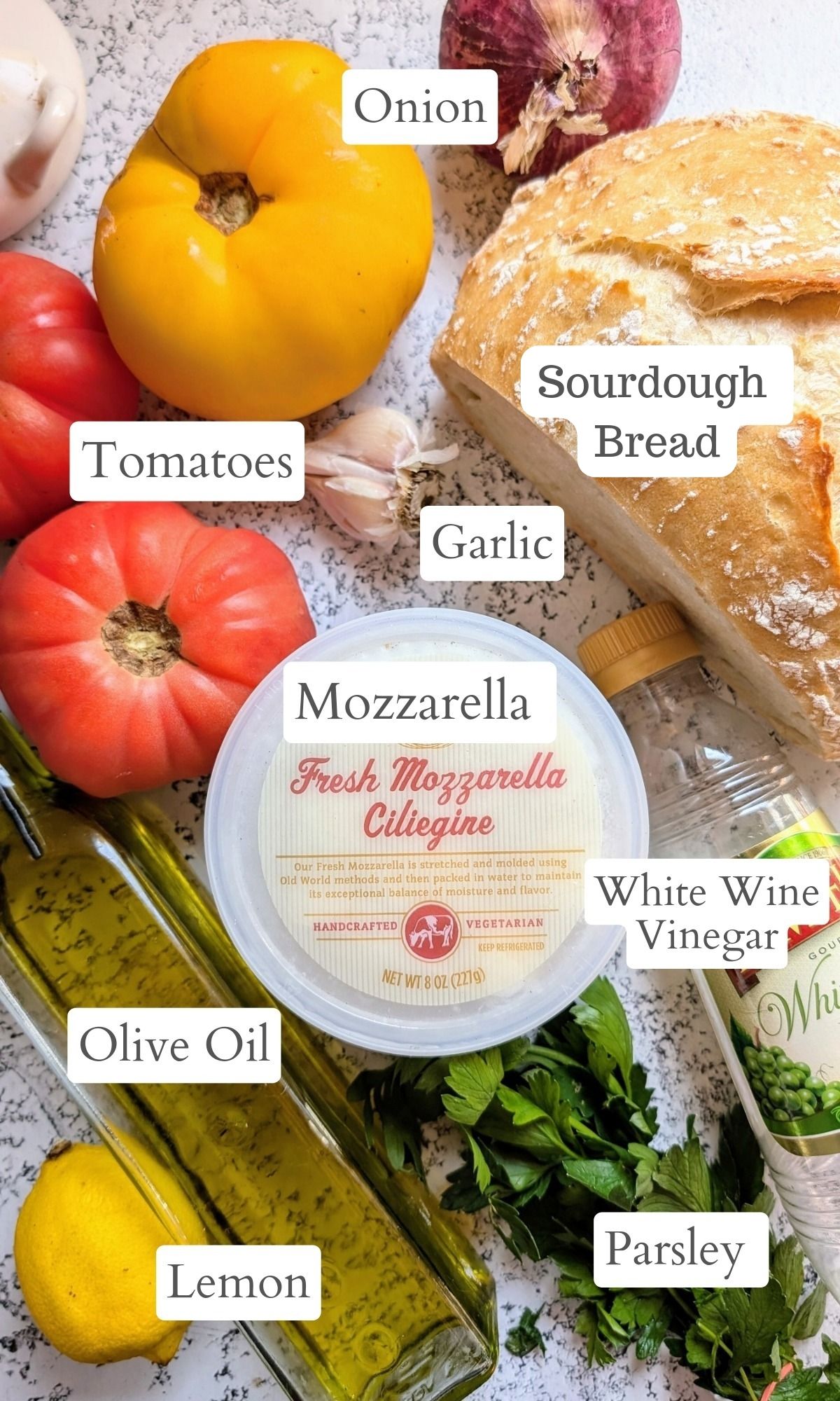 ingredients for panzanella with sourdough bread like fresh summer tomatoes, mozzarella cheese, parsley, garlic, and olive oil.