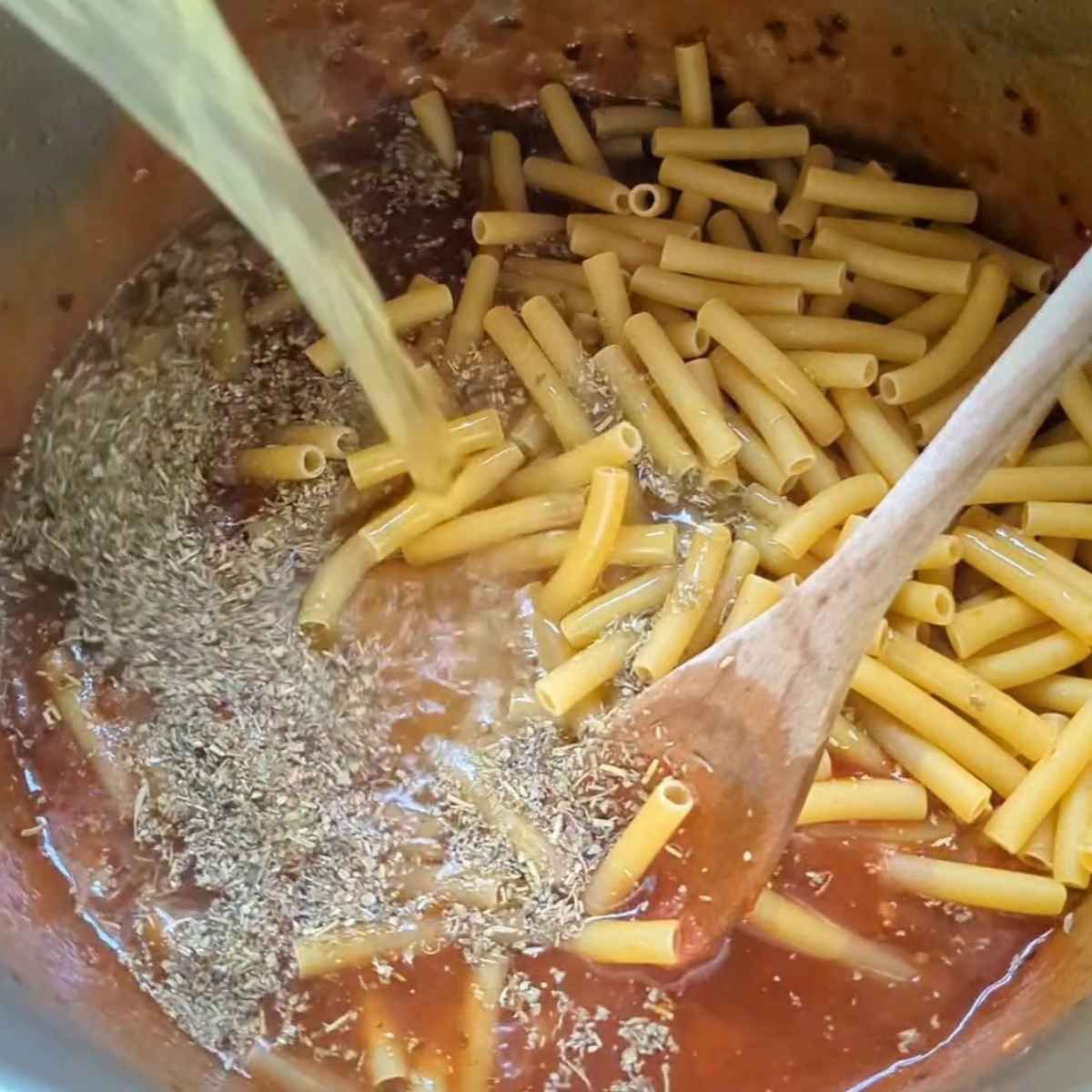 instant pot with ziti noodles and tomato paste with vegetbale stock or broth being poured into the pot.