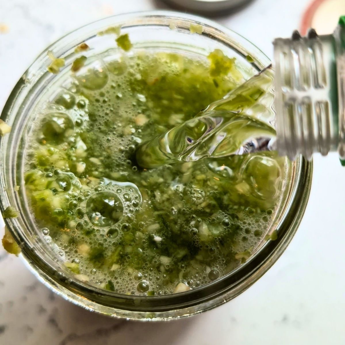 a jar of jalapeno mash with garlic and a hand pouring white vinegar into the jar to make hot sauce.