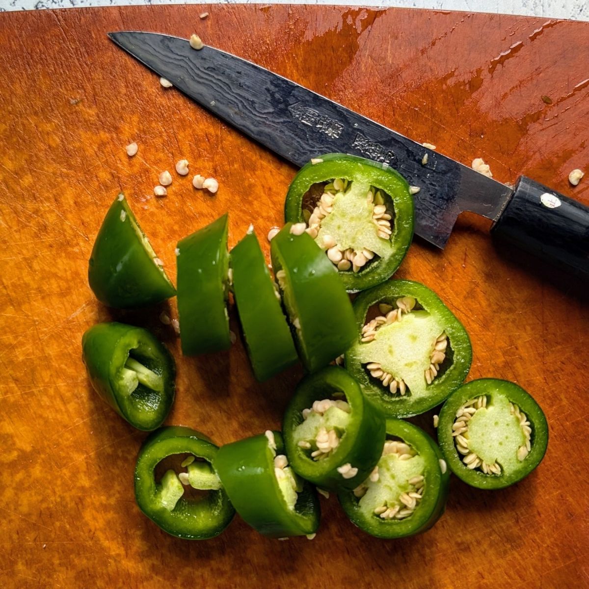 sliced jalapeno peppers on a cutting board to make homemade green hot sauce.